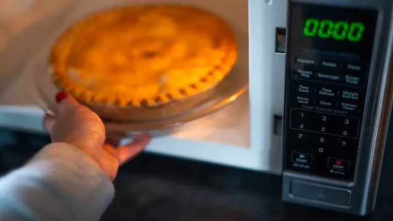 Manicured hand removing pie from microwave.
